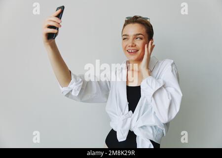 Une jeune fille blogger prend des photos et des pousses. elle-même sur la vidéo sur son téléphone pour le contenu de médias sociaux, blogueur vidéo, se selfie contre un mur blanc avec Banque D'Images