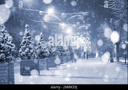 Rue de la ville pendant les chutes de neige pendant la nuit d'hiver. Beaucoup d'arbres de Noël décorés, éclairage, décoration sur la rue. Fête de Noël du nouvel an. Lanternes sur les arbres. Couleur bleue Banque D'Images