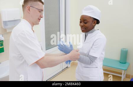 le médecin aide le chirurgien à mettre un gant dans la salle d'opération, les mains de nombreux médecins sont dans des gants. Banque D'Images