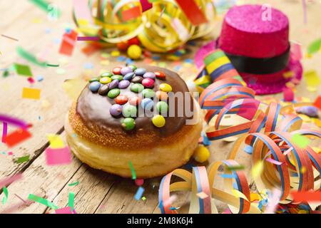 Krapfen, berliner ou Carnival donut d'Allemagne avec du sucre glace sur une surface en bois clair avec des confettis et des banderoles sur elle - fond pour un carni Banque D'Images