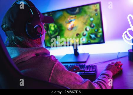 Professionnelle féminine Gamer joue la stratégie concentrée jeu vidéo en ligne sur son ordinateur personnel. Salle éclairée par des néons dans un style arcade rétro. Banque D'Images