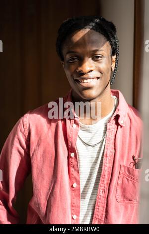 Joyeux Africain américain avec des cheveux tresses regardant la caméra souriant debout près de la fenêtre à la maison. Banque D'Images