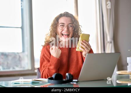 Jeune femme heureuse et excitée étudiante tenant un téléphone mobile célébrant la victoire. Banque D'Images