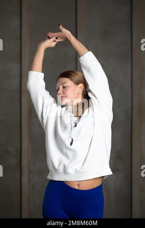 Une femme sportive étire le bras et l'épaule tout en se tenant debout. Instructeur Pilates. Étirement. Banque D'Images