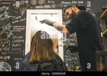 vue arrière d'une femme brune assise sur la chaise et d'un coiffeur tenant un grand peigne. Photo de haute qualité Banque D'Images