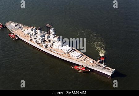 Une vue aérienne à tribord de l'arc du cuirassé WISCONSIN (BB-64) étant manoeuvré par six remorqueurs commerciaux alors que le navire est déplacé au chantier naval de Norfolk à Portsmouth pour un entreposage de réserve prêt. Le navire a été remorqué de Philadelphie quand cette installation a été fermée. Base: Hampton roadstead État: Virginie (va) pays: Etats-Unis d'Amérique (USA) Banque D'Images