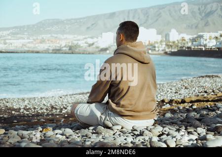 Un homme dans un sweat à capuche beige est assis sur le fond de la mer. Un gars marche sur la plage et apprécie la vue, le bonheur de voyager dans le summe Banque D'Images