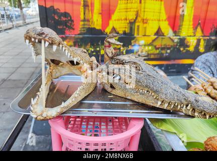 Viande de crocodile à vendre, brochée sur des bâtonnets de bambou, les têtes séchées sur un plateau d'argent, utilisé pour annoncer la viande populaire thaï, à vendre près d'une tente Banque D'Images