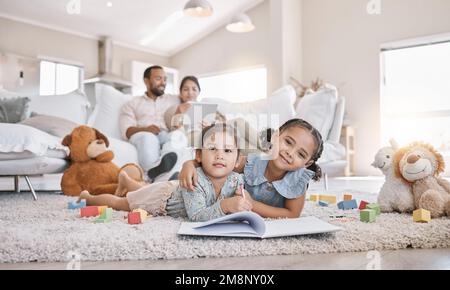 Deux petites filles dessin avec des crayons de couleur couché sur le sol de la salle de séjour avec leurs parents se détendant sur le canapé. Petits enfants sœurs frères et sœurs Banque D'Images