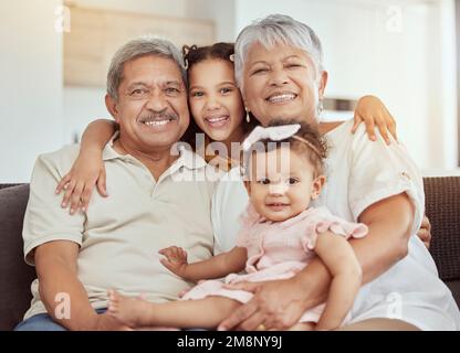 Portrait de grands-parents de race mixte appréciant le week-end avec les petites-filles dans le salon à la maison. Souriant hispanique filles se liant avec grand-mère et Banque D'Images