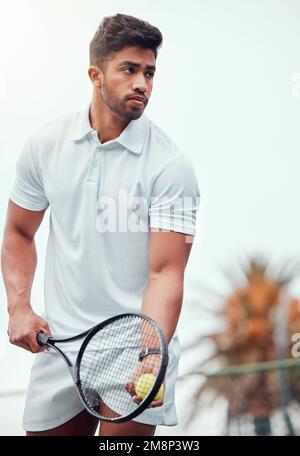 Un joueur de tennis indien sérieux se prépare à servir seul sur le court. Un athlète ethnique tenant une raquette et un ballon pendant le match. Actif et ciblé Banque D'Images