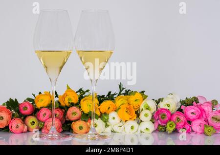 Deux verres de vin blanc avec fleurs de ranunculus colorées sur fond blanc pour le concept de gastronomie de Valentines. Banque D'Images