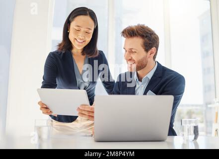 Deux jeunes collègues heureux et divers travaillant ensemble sur une tablette numérique dans un bureau. Femme d'affaires asiatique confiante et homme d'affaires caucasien souriant Banque D'Images