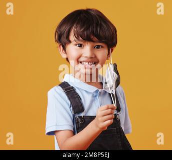 Portrait d'un adorable petit garçon asiatique heureux tout en portant un masque contre un fond orange studio copyspace. Un enfant souriant retire son masque Banque D'Images