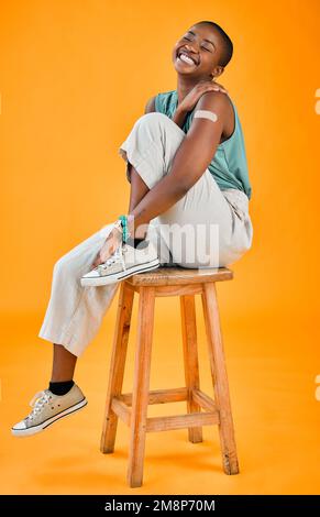 Femme vaccinée Covid afro-américaine montrant du plâtre sur le bras et souriant. Modèle noir sur toute la longueur isolé sur fond de studio jaune avec Banque D'Images