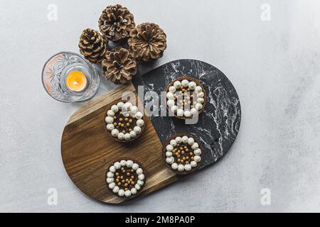 Vue de haut en bas de quatre mini-tartes de desserts au chocolat sur un plateau minimaliste en bois et en pierre à côté de la bougie et des pommes de pin. Desserts festifs. Tir horizontal . Photo de haute qualité Banque D'Images