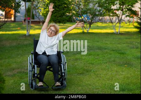 Femme caucasienne âgée faisant des exercices en étant assise dans un fauteuil roulant à l'extérieur. Banque D'Images