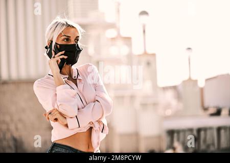Femme avec masque de visage regardant loin en parlant au téléphone à l'extérieur. Banque D'Images