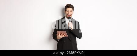 Image d'un homme de qualité, qui fait un discours, divertit les personnes en fête, tient un micro et une tablette numérique, debout sur fond blanc Banque D'Images