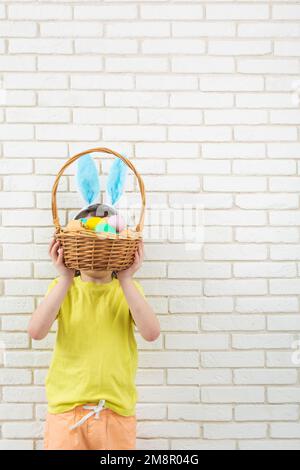 Garçon aux oreilles de lapin de Pâques avec panier en osier et œufs colorés. Copier l'espace Banque D'Images