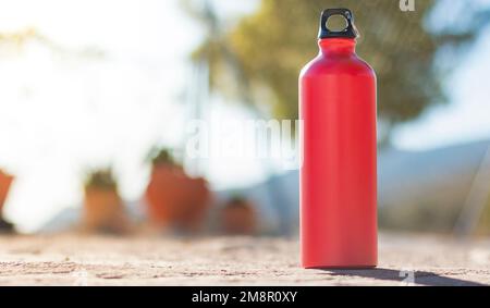 Une bouteille d'eau en aluminium rouge avec bouchon à vis noir sur une surface en ciment gris à l'extérieur. L'arrière-plan n'est pas mis au point. Banque D'Images