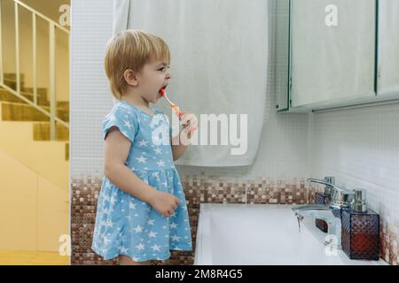 Une petite fille se brosse les dents dans la salle de bains. Banque D'Images