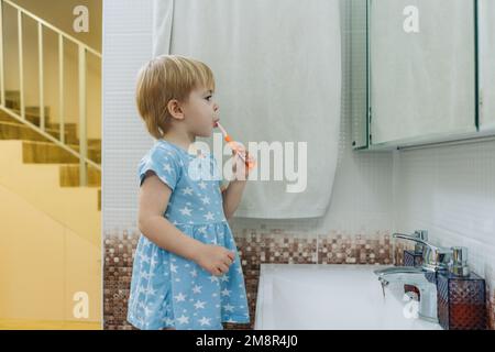 Une petite fille se brosse les dents dans la salle de bains. Banque D'Images