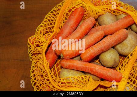 Sac en maille orange. Vue de dessus. Gros plan. Légumes frais du marché agricole. Pommes de terre crues, carottes crues. Consommation consciente, sac réutilisable, Banque D'Images