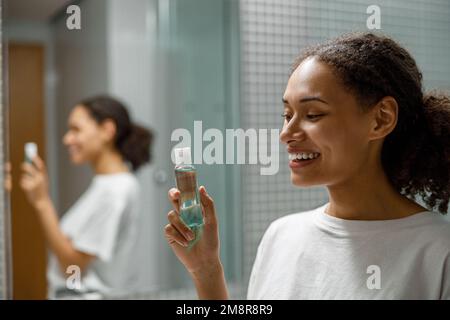 Bonne fille africaine tenant des cosmétiques naturels de soin de peau ou de soin du corps debout dans la salle de bains Banque D'Images