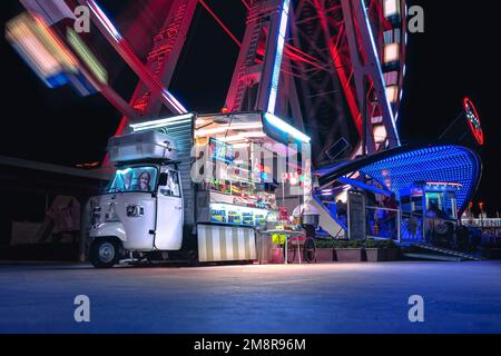 RIMINI, ITALIE - 25 août 2020: Photographie nocturne colorée de voiture de bonbon lumineux sous la roue de ferris sur la place touristique populaire de Rimini Italie. Banque D'Images