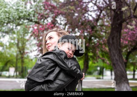Jeune mère maman tenant son petit fils garçon enfant sous des arbres en fleurs Banque D'Images