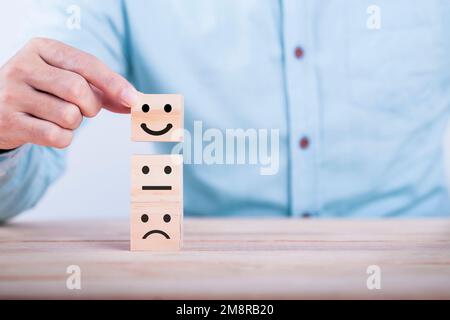 Homme d'affaires choisit un sourire émoticône icônes face heureux symbole sur bloc de bois , Services et le concept d'enquête de satisfaction client Banque D'Images