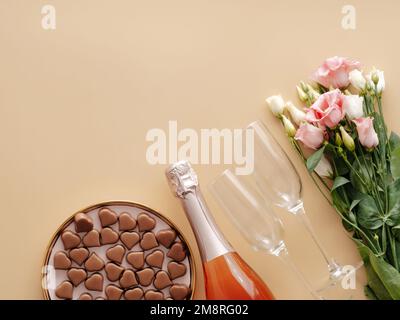 Concept de la Saint-Valentin sur fond jaune pastel. Bouteille de champagne rose, verres, bouqet de fleurs et confiseries romantiques au chocolat en forme de coeur.CopySpace.fond beige Champagne.Topview platlay Banque D'Images