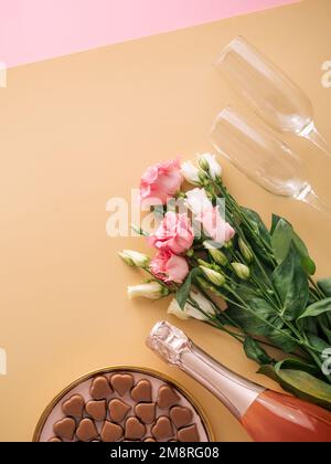 Concept de la Saint-Valentin sur fond jaune pastel. Bouteille de champagne rose, verres, bouqet de fleurs et confiseries romantiques au chocolat en forme de coeur.CopySpace.fond beige Champagne.Topview platlay Banque D'Images