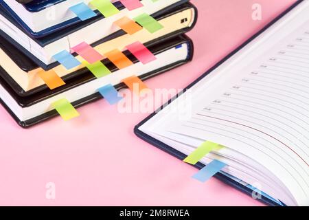 Gros plan d'un bloc-notes ouvert avec des marqueurs de page adhésifs colorés sur l'arrière-plan d'une pile de blocs-notes de bureau Banque D'Images