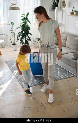 La famille mère et l'enfant quittent la maison avec une valise en voyage ou en vacances Banque D'Images