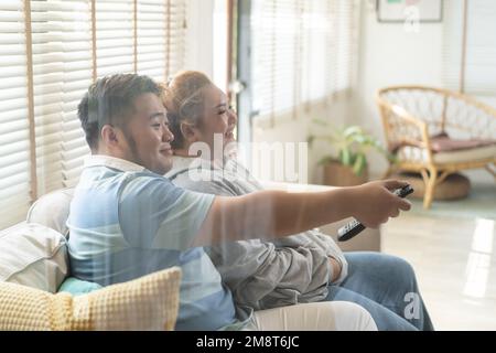 Un jeune couple asiatique de chubby regarde une série télévisée et un film sur le canapé dans le salon. Homme et femme qui s'amusent ensemble à la maison. Les gens rient et sourient ensemble Banque D'Images