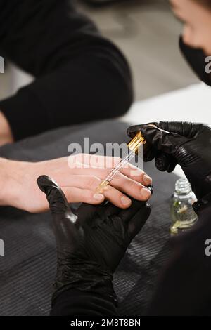 Manucure masculine. Vue rapprochée du maître de manucure féminin qui fait la manucure pour l'homme. Guy soins des mains au salon de beauté. Huile de Cuticula Banque D'Images