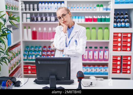 Jeune femme caucasienne travaillant à la pharmacie en pharmacie pensant à la fatigue et s'ennuyer avec des problèmes de dépression avec les bras croisés. Banque D'Images