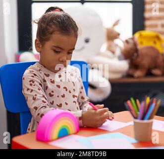 Adorable étudiante hispanique de fille assise sur table de dessin sur papier à la maternelle Banque D'Images