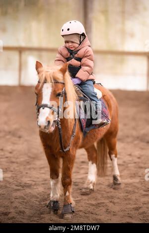 Leçon de équitation pour les petits enfants. Une jeune fille de trois ans fait du poney et fait des exercices Banque D'Images