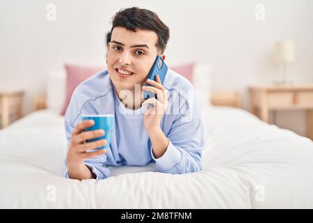 Jeune homme non binaire parlant sur le smartphone buvant du café Banque D'Images