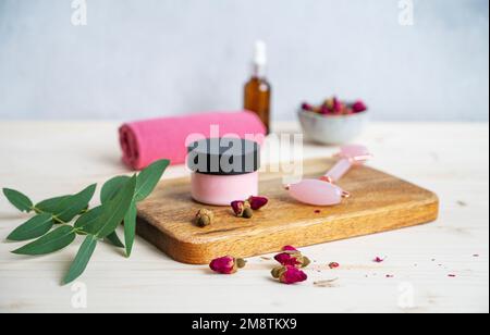 Cosmétiques de soin du visage et du corps avec rose et eucalyptus. Le concept de soins spa avec crème et masseur de gua sha. Copier l'espace Banque D'Images