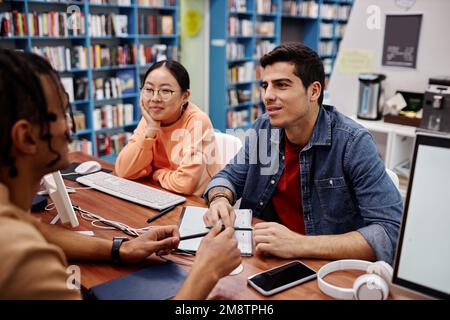 Groupe multiethnique de jeunes étudiant ensemble dans la bibliothèque du collège et discutant des devoirs Banque D'Images