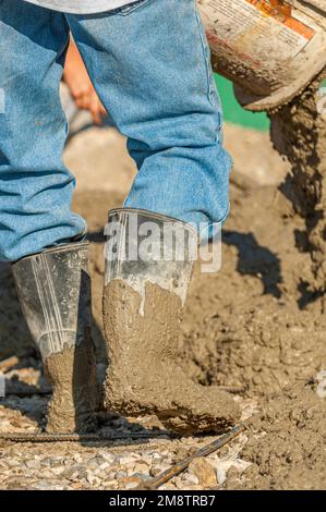 Ouvriers qui déversent une bouillie de béton sur un lit de gravier et d'armature à un chantier de construction Banque D'Images