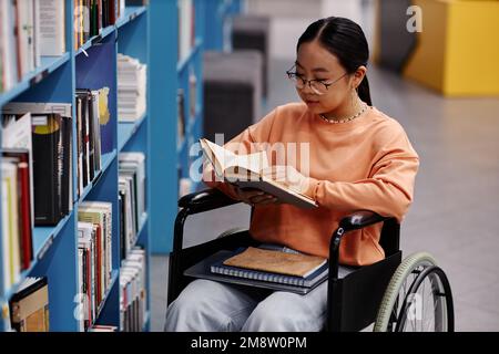 Portrait à grand angle de fille asiatique avec handicap dans le cadre de bibliothèque d'université livres de lecture Banque D'Images