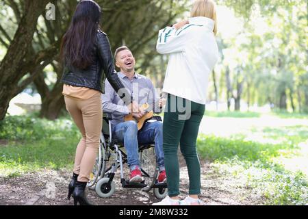 Heureux homme décédé en fauteuil roulant jouant ukulele pour ses amis dans le parc. Banque D'Images