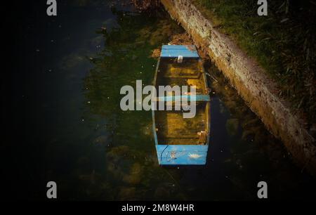 Un petit bateau naufragé couvert de mousse, vu dans une rivière sale Banque D'Images