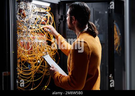 Vue latérale d'un technicien réseau travaillant avec des serveurs et des câbles de connexion Banque D'Images