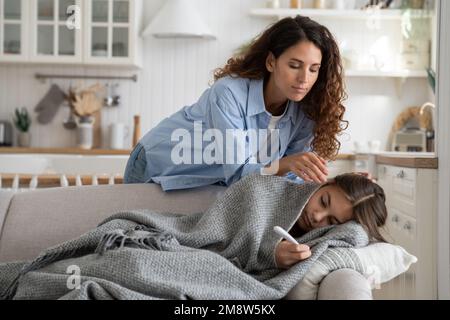 Parent inquiet mère prenant soin de l'enfant malade couché dans le lit sous couverture avec fièvre à la maison Banque D'Images